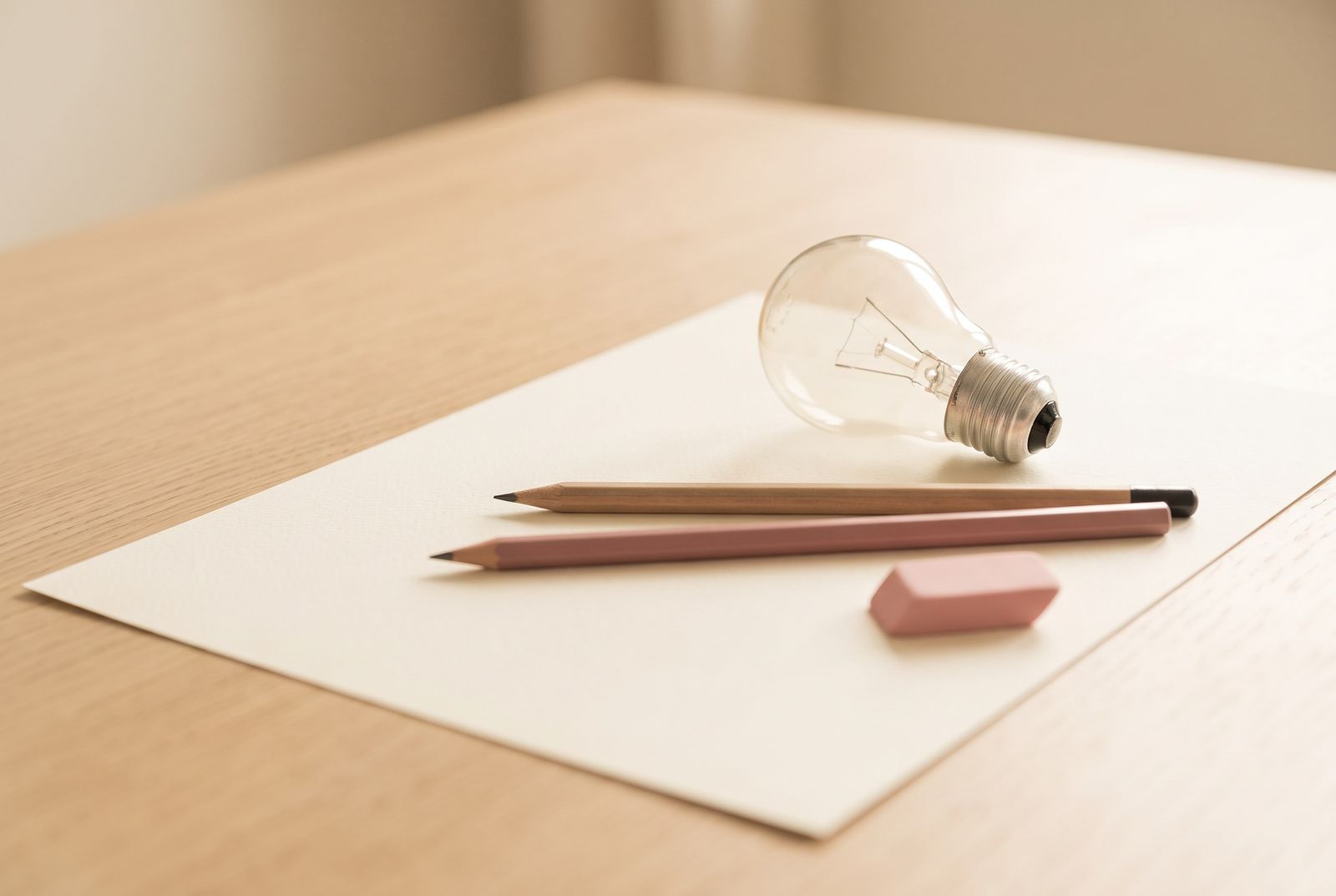 Cream paper, light bulb and pencils on a light oak desk