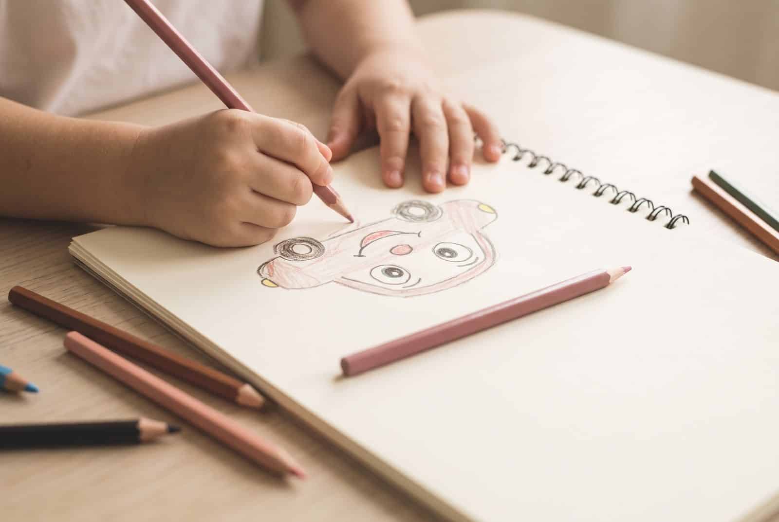 Mains d'enfant dessinant un personnage imaginaire aux crayons de couleur