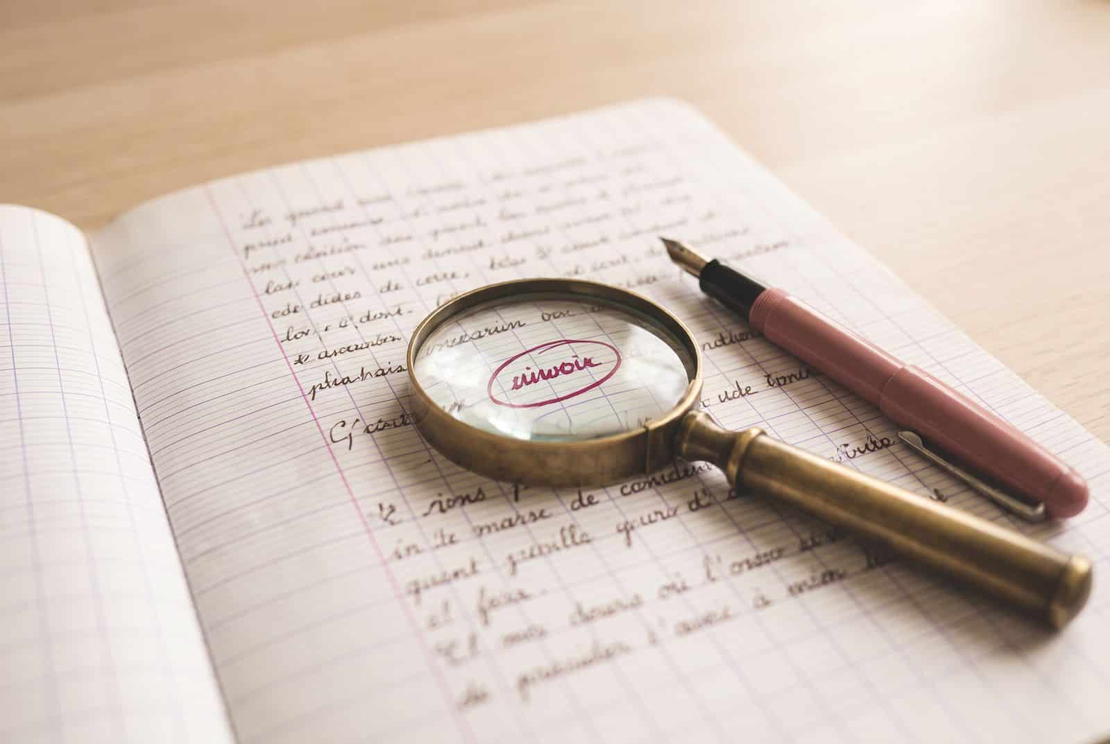 Cahier de dictée avec une faute entourée en rouge sous une loupe