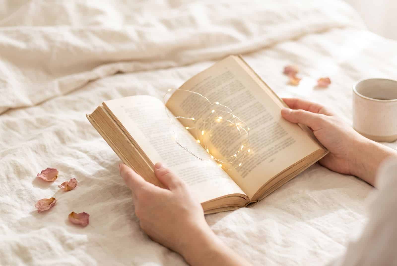 Open book with glowing fairy lights held in a woman's hands on cream linen